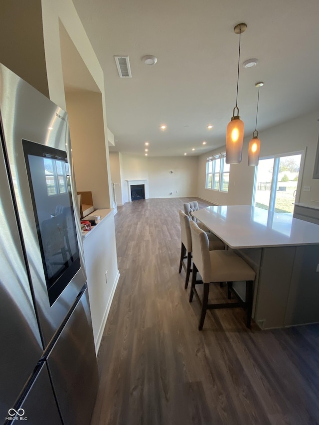 kitchen featuring dark hardwood / wood-style floors, stainless steel fridge, hanging light fixtures, and a breakfast bar