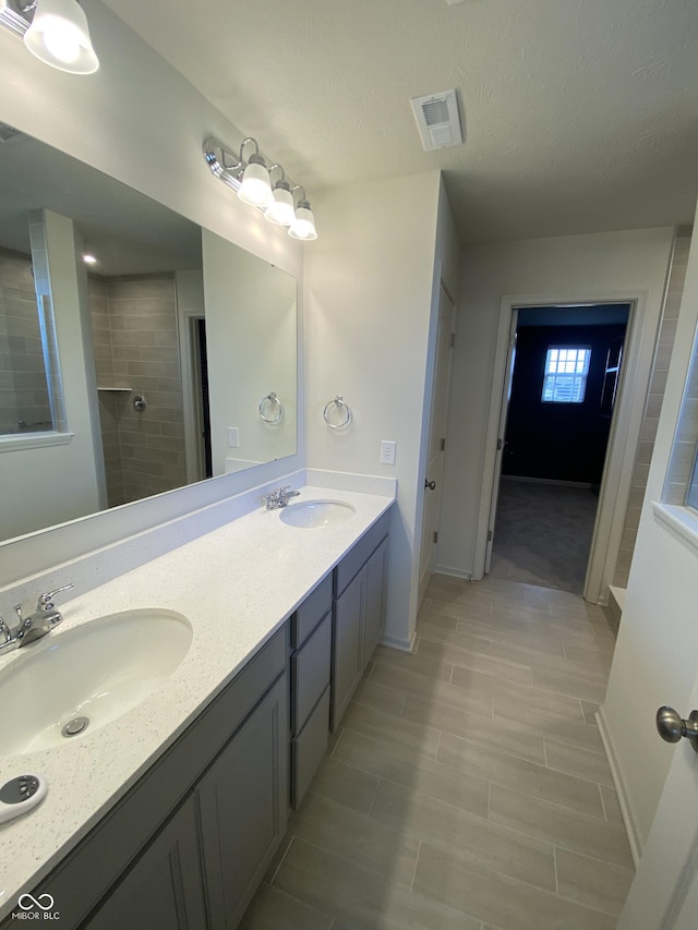 bathroom featuring a textured ceiling, vanity, and tiled shower