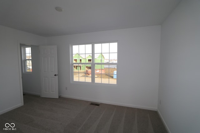 spare room featuring plenty of natural light and dark carpet