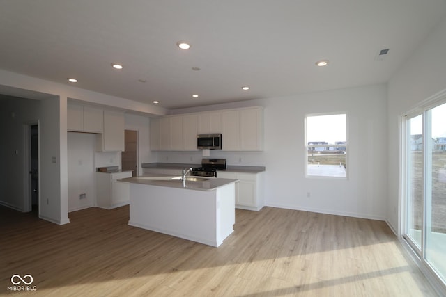 kitchen featuring sink, white cabinetry, stainless steel appliances, an island with sink, and light wood-type flooring