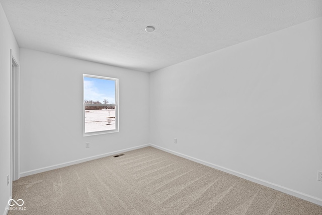 spare room featuring light carpet, a textured ceiling, visible vents, and baseboards