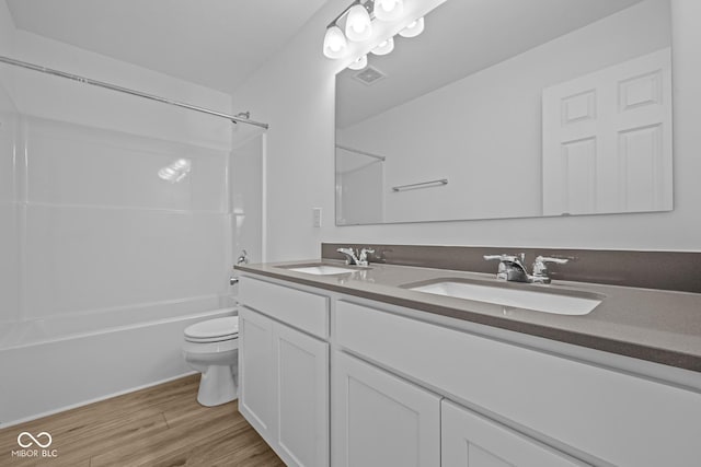 full bathroom with toilet, double vanity, a sink, and wood finished floors