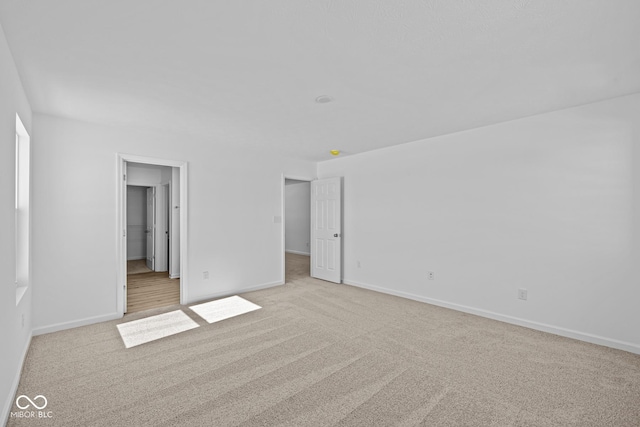 unfurnished bedroom with baseboards, a walk in closet, and light colored carpet