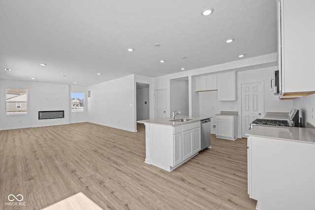 kitchen with white cabinets, a glass covered fireplace, appliances with stainless steel finishes, light wood-type flooring, and a sink