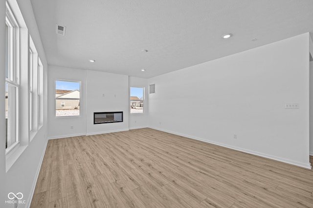 unfurnished living room with light wood finished floors, baseboards, visible vents, and a glass covered fireplace