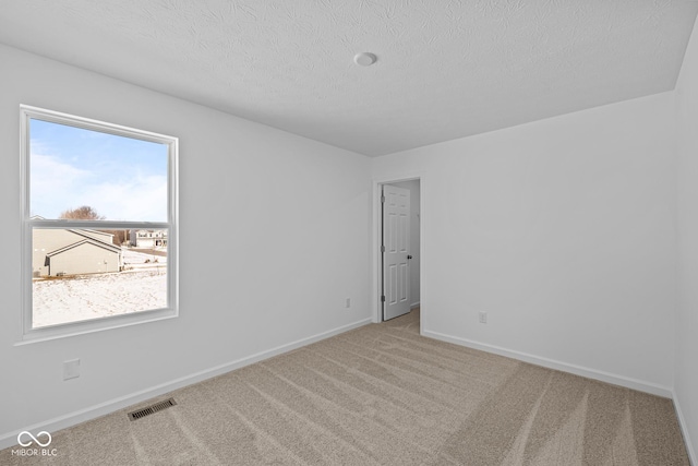 carpeted empty room featuring baseboards, visible vents, and a textured ceiling