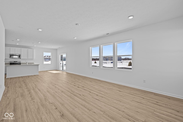 unfurnished living room with a textured ceiling, recessed lighting, light wood-style flooring, and baseboards