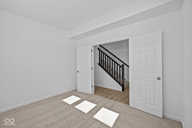 carpeted spare room with stairs and baseboards