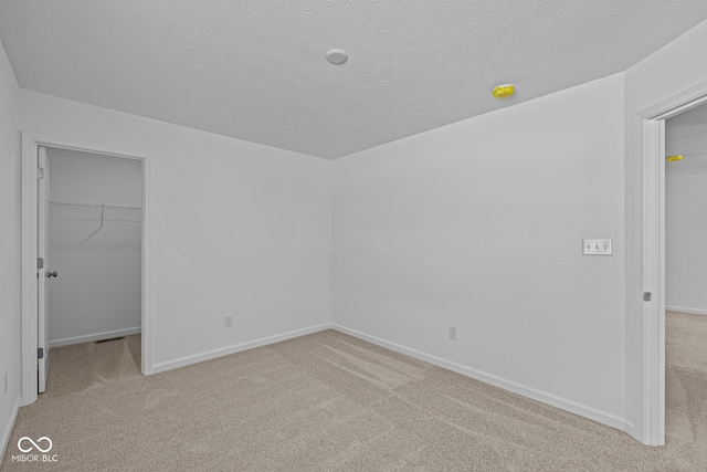 unfurnished bedroom with a textured ceiling, a closet, carpet, and a walk in closet