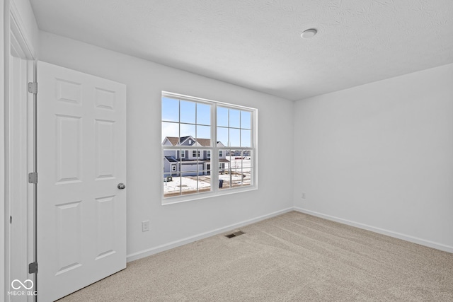 spare room featuring light carpet, a textured ceiling, visible vents, and baseboards