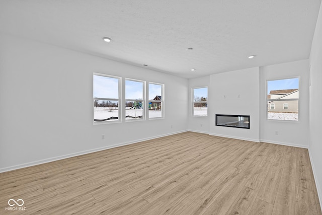 unfurnished living room with a textured ceiling, light wood-type flooring, a glass covered fireplace, and baseboards