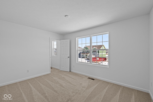 carpeted spare room featuring a textured ceiling, visible vents, and baseboards