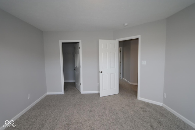 unfurnished bedroom with a walk in closet, a closet, and light carpet