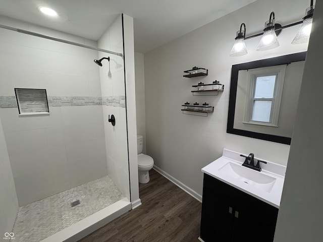 bathroom with tiled shower, hardwood / wood-style floors, vanity, and toilet