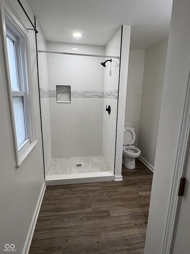 bathroom featuring hardwood / wood-style flooring, plenty of natural light, toilet, and tiled shower