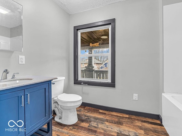 bathroom featuring a washtub, hardwood / wood-style floors, toilet, vanity, and a textured ceiling