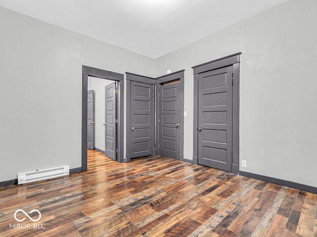 unfurnished bedroom with a baseboard heating unit and dark hardwood / wood-style flooring