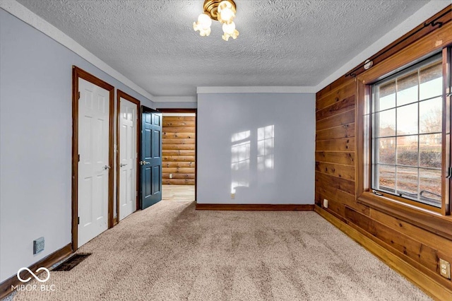 unfurnished bedroom featuring carpet flooring, a textured ceiling, ensuite bath, and wood walls