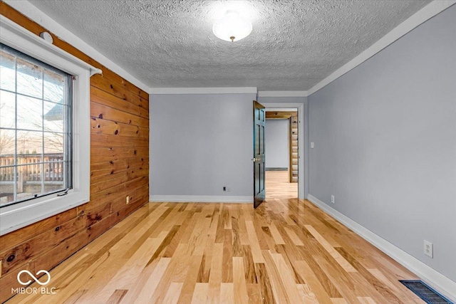 empty room with wood walls, light hardwood / wood-style floors, and a textured ceiling