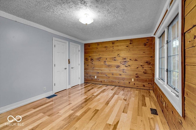 empty room with a textured ceiling, light wood-type flooring, and wood walls