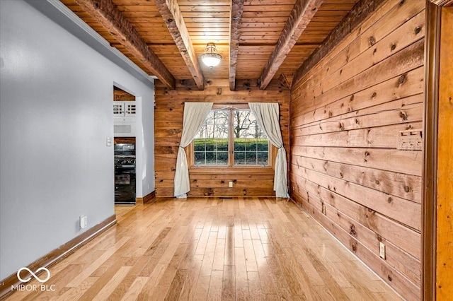 empty room with beam ceiling, light wood-type flooring, wooden walls, and wooden ceiling