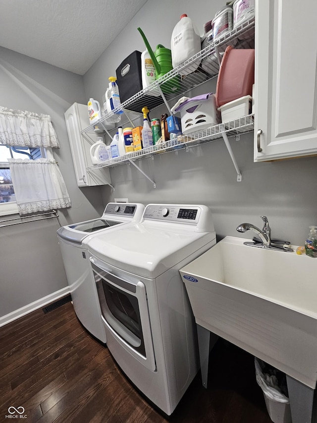 clothes washing area featuring washer and clothes dryer, dark hardwood / wood-style flooring, cabinets, and a textured ceiling