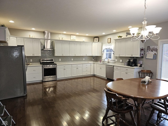 kitchen featuring pendant lighting, dark wood-type flooring, wall chimney range hood, white cabinetry, and stainless steel appliances