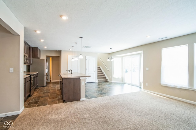 kitchen featuring appliances with stainless steel finishes, dark brown cabinets, a kitchen island with sink, and pendant lighting