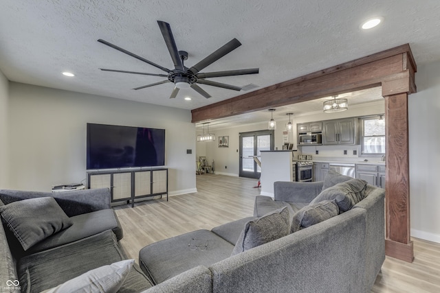 living room featuring beamed ceiling, a textured ceiling, light wood-type flooring, and ceiling fan with notable chandelier