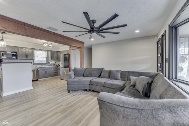 living room featuring sink, ceiling fan, a textured ceiling, beamed ceiling, and light hardwood / wood-style floors