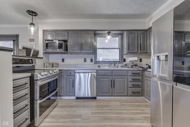 kitchen featuring ornamental molding, gray cabinetry, stainless steel appliances, pendant lighting, and light hardwood / wood-style floors