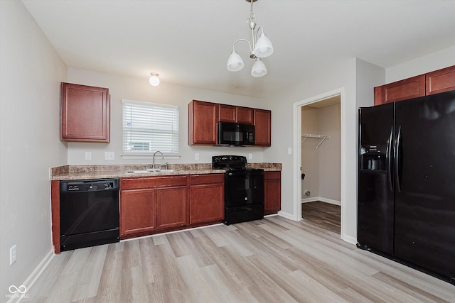 kitchen with light wood-type flooring, sink, black appliances, decorative light fixtures, and a chandelier