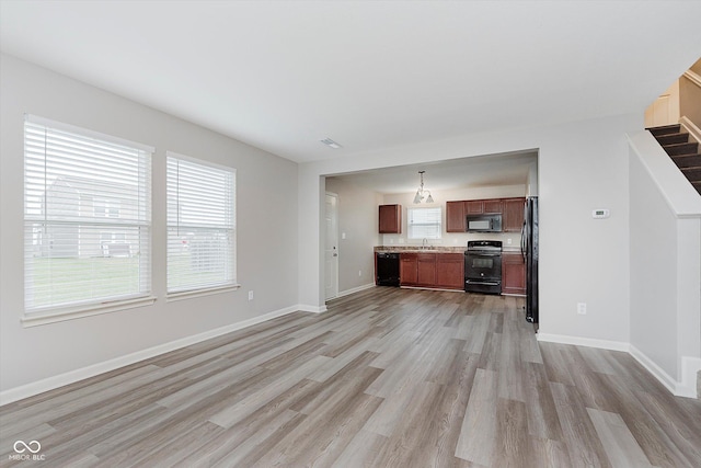 kitchen featuring a wealth of natural light, pendant lighting, black appliances, and light hardwood / wood-style flooring