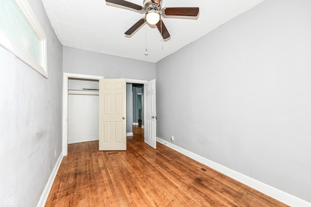 unfurnished bedroom featuring a closet, a textured ceiling, hardwood / wood-style flooring, and ceiling fan