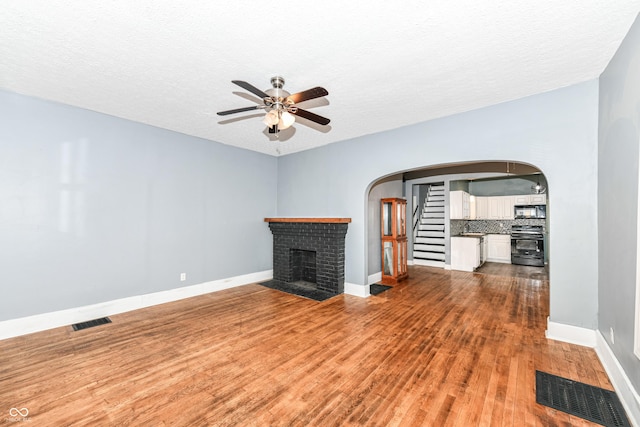 3458 N Kenwood Ave, Indianapolis, IN 46208 - unfurnished living room featuring arched walkways, ceiling fan, wood finished floors, a fireplace, and a textured ceiling