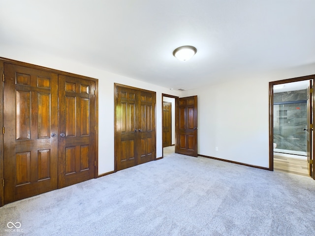 unfurnished bedroom featuring ensuite bath, light carpet, and multiple closets