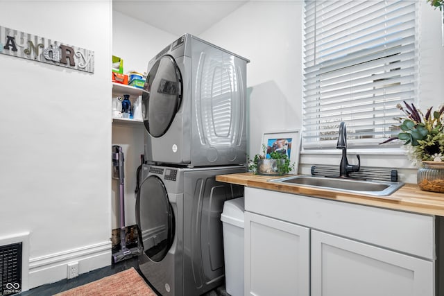 clothes washing area featuring cabinets, sink, and stacked washer / dryer