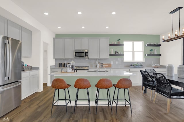 kitchen featuring a center island with sink, sink, appliances with stainless steel finishes, decorative light fixtures, and white cabinetry