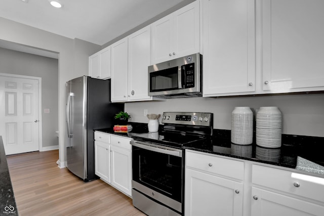 kitchen featuring white cabinets, light wood-type flooring, stainless steel appliances, and dark stone counters