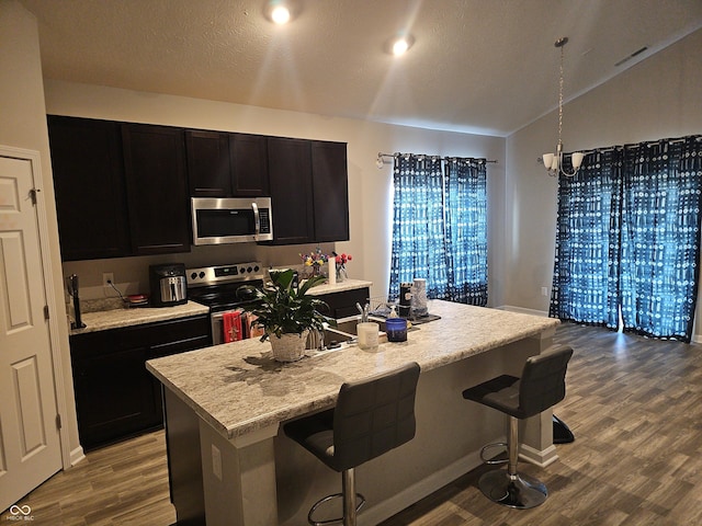 kitchen with appliances with stainless steel finishes, a breakfast bar, a kitchen island with sink, wood-type flooring, and decorative light fixtures