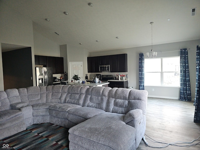 living room with a notable chandelier, light wood-type flooring, and high vaulted ceiling