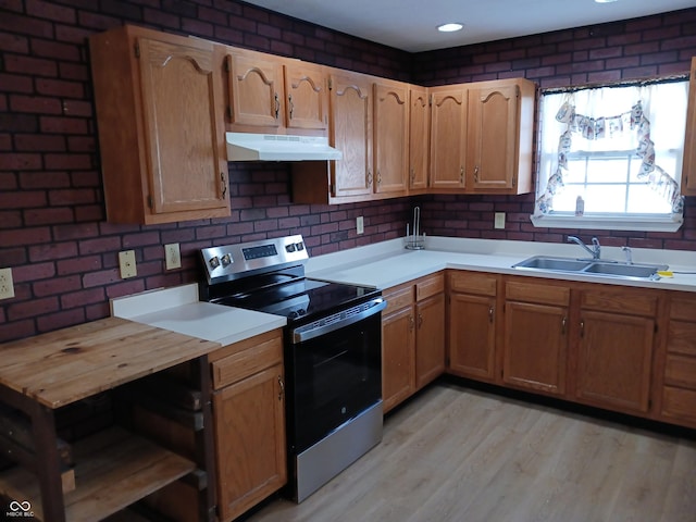 kitchen featuring sink, stainless steel range with electric cooktop, light hardwood / wood-style floors, and brick wall