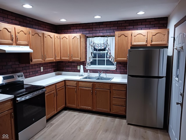 kitchen with brick wall, stainless steel appliances, light hardwood / wood-style floors, and sink