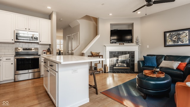 kitchen with a tile fireplace, white cabinets, appliances with stainless steel finishes, a kitchen island, and a breakfast bar area