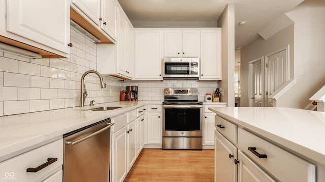 kitchen with sink, tasteful backsplash, light hardwood / wood-style flooring, white cabinets, and appliances with stainless steel finishes