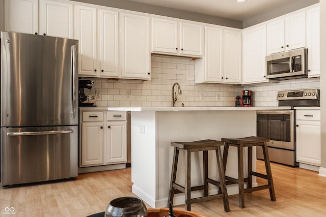 kitchen featuring appliances with stainless steel finishes, sink, light hardwood / wood-style flooring, white cabinets, and a breakfast bar area