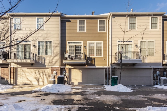 snow covered rear of property featuring cooling unit and a garage