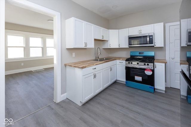 kitchen featuring wood counters, range with gas cooktop, white cabinetry, and sink