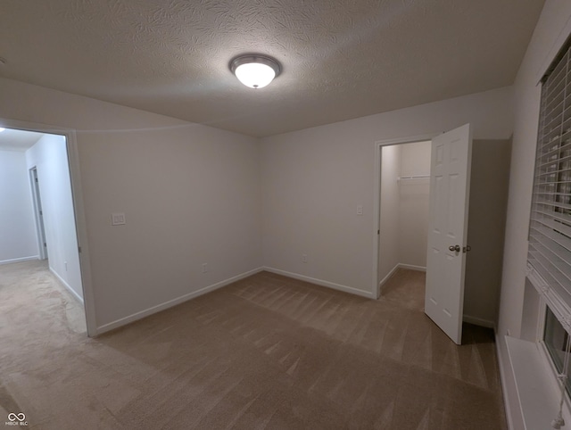 unfurnished bedroom with light colored carpet, a spacious closet, a closet, and a textured ceiling