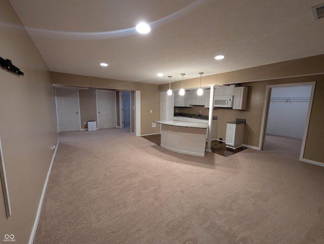 interior space featuring white cabinetry, hanging light fixtures, light carpet, and a kitchen island